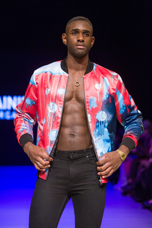 Male model wearing RAINING COWS ‘Unmasked United Again’ bomber jacket by Morgan Sheardown, red and blue Silk with cow and rain motif, styled with black pants, posing on the runway.